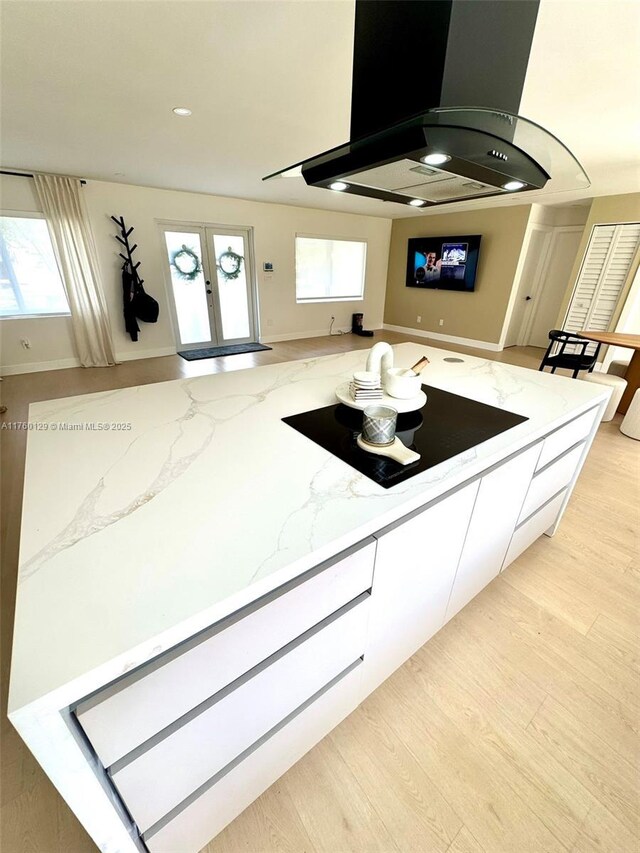 kitchen featuring light stone countertops, light wood-style flooring, french doors, black electric cooktop, and island range hood