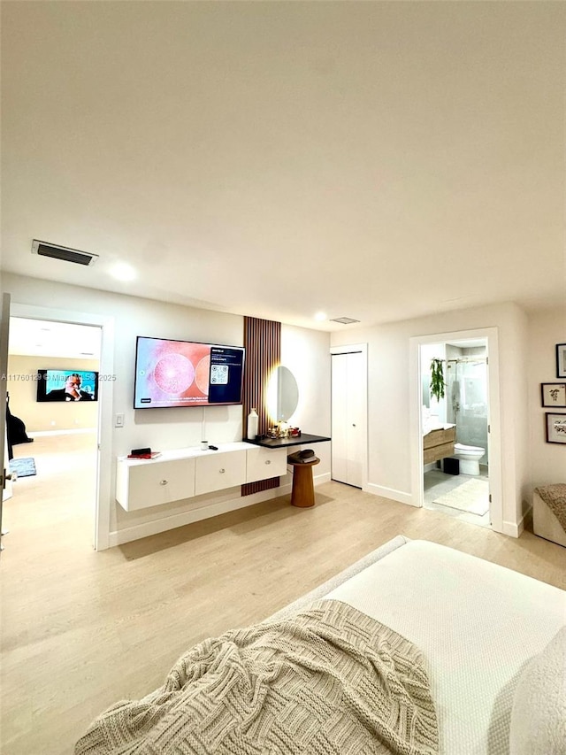 bedroom featuring visible vents, baseboards, ensuite bathroom, and light wood finished floors