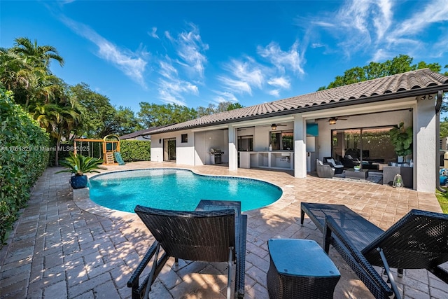 outdoor pool with a playground, fence, outdoor lounge area, a patio area, and a grill