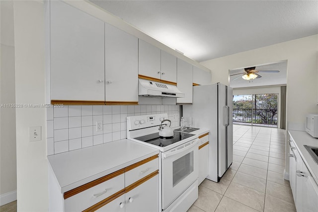 kitchen with under cabinet range hood, backsplash, white appliances, light countertops, and light tile patterned floors