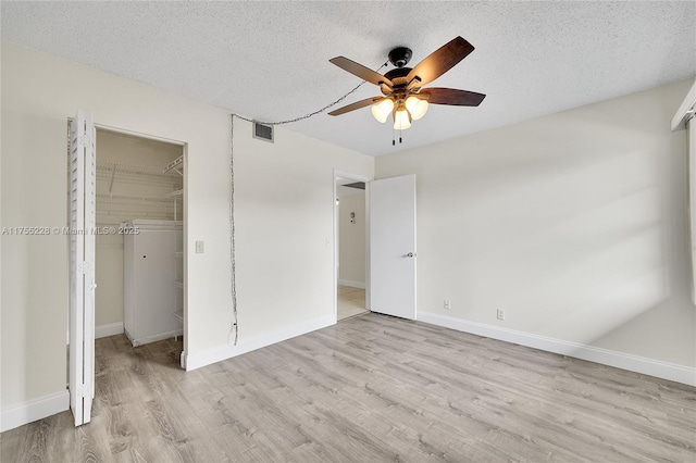 unfurnished bedroom with a textured ceiling, a walk in closet, visible vents, and light wood-type flooring