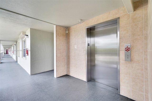 corridor featuring elevator, a textured ceiling, and tile walls