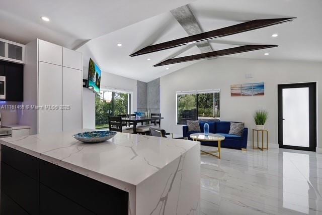 kitchen featuring beam ceiling, modern cabinets, open floor plan, a center island, and light stone countertops