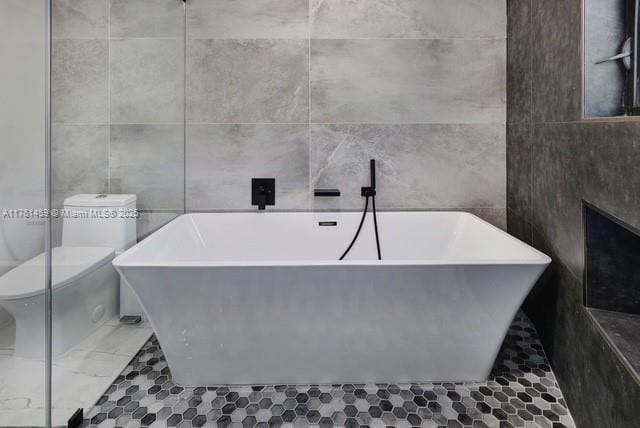 bathroom featuring a soaking tub, toilet, and tile walls