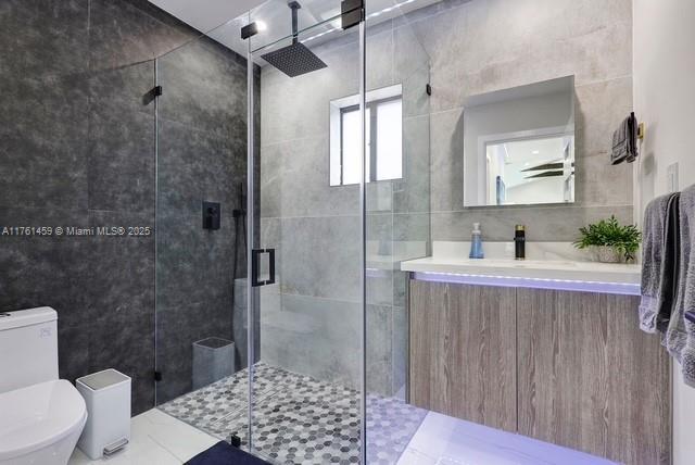 full bathroom featuring toilet, tile walls, a stall shower, and vanity