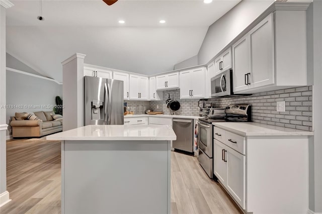 kitchen with a kitchen island, vaulted ceiling, decorative backsplash, light wood-style flooring, and stainless steel appliances