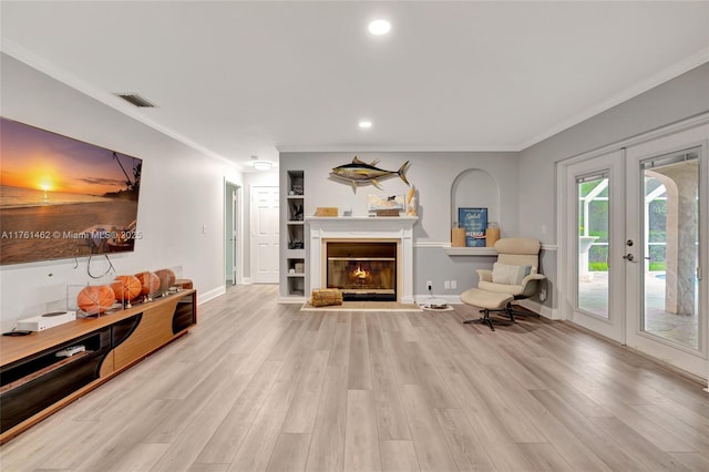 living area with visible vents, crown molding, french doors, wood finished floors, and a glass covered fireplace