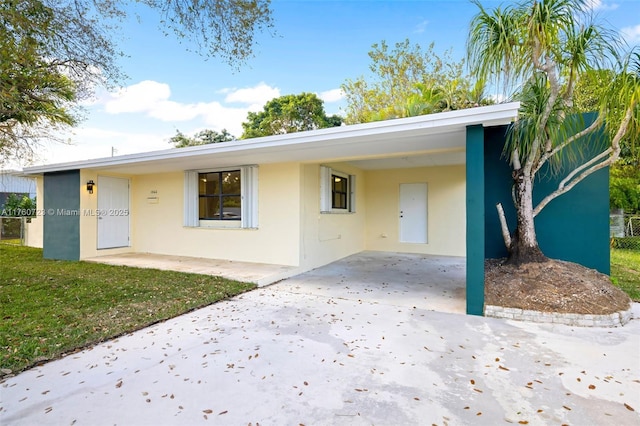 view of front of house with stucco siding, driveway, a carport, and a front yard