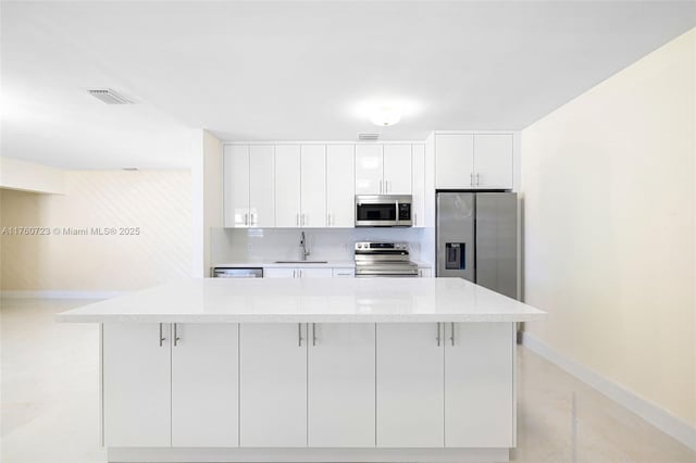 kitchen featuring a sink, a kitchen island, appliances with stainless steel finishes, white cabinets, and baseboards