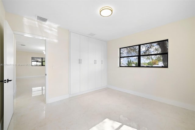 unfurnished bedroom with multiple windows, baseboards, visible vents, and a closet