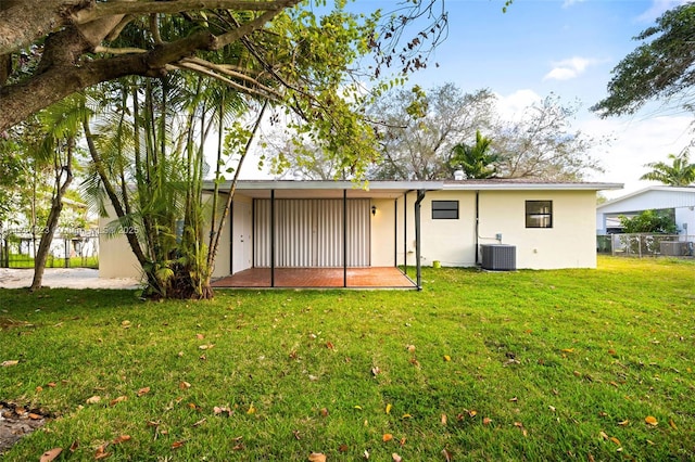 rear view of property featuring a yard, fence, central AC, and stucco siding