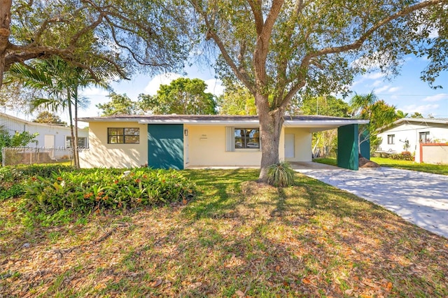 view of front facade featuring an attached carport, fence, a front yard, stucco siding, and driveway