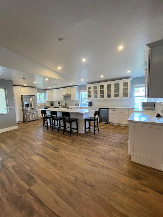 kitchen featuring beverage cooler, white cabinets, stainless steel fridge with ice dispenser, and vaulted ceiling