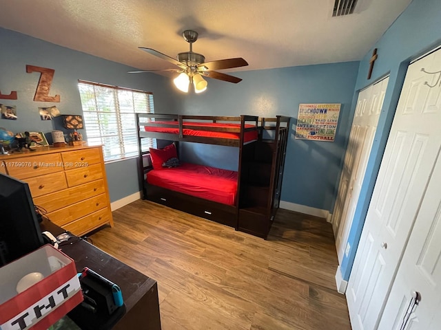 bedroom with wood finished floors, visible vents, two closets, and baseboards