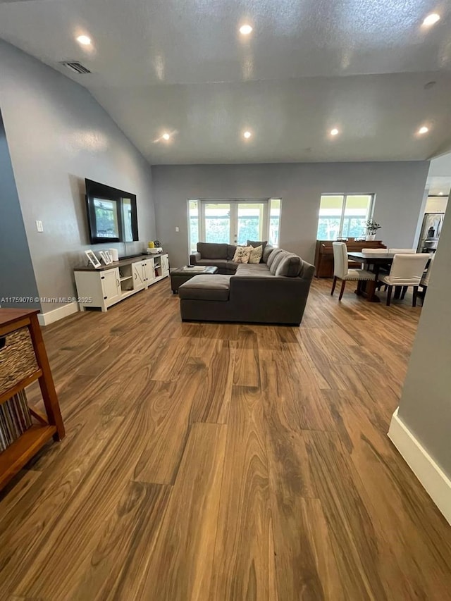 living room featuring visible vents, baseboards, lofted ceiling, wood finished floors, and a textured ceiling