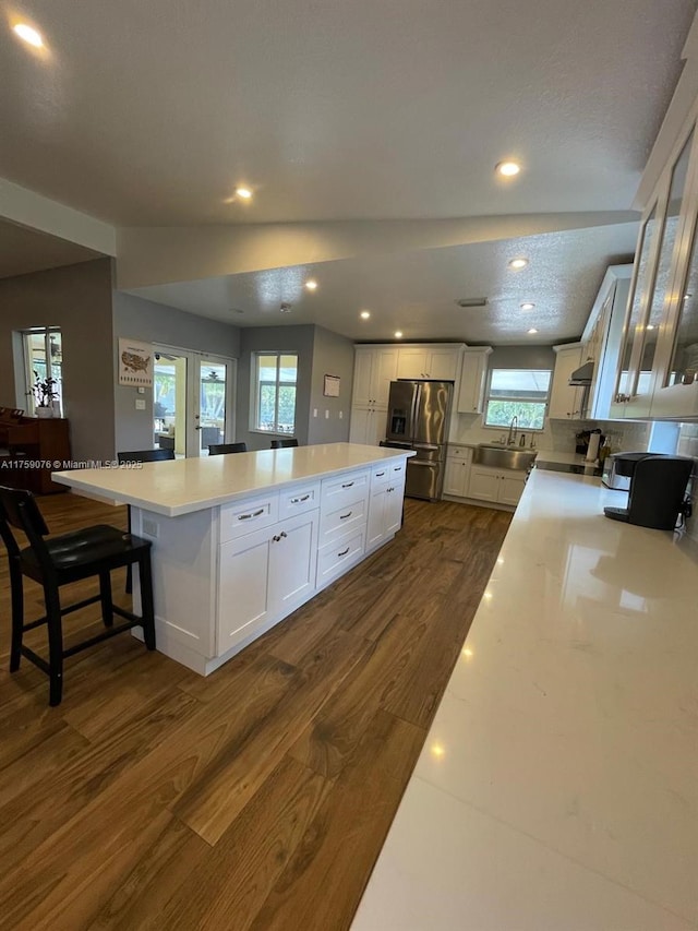 kitchen with stainless steel fridge with ice dispenser, dark wood-type flooring, a large island, light countertops, and white cabinetry