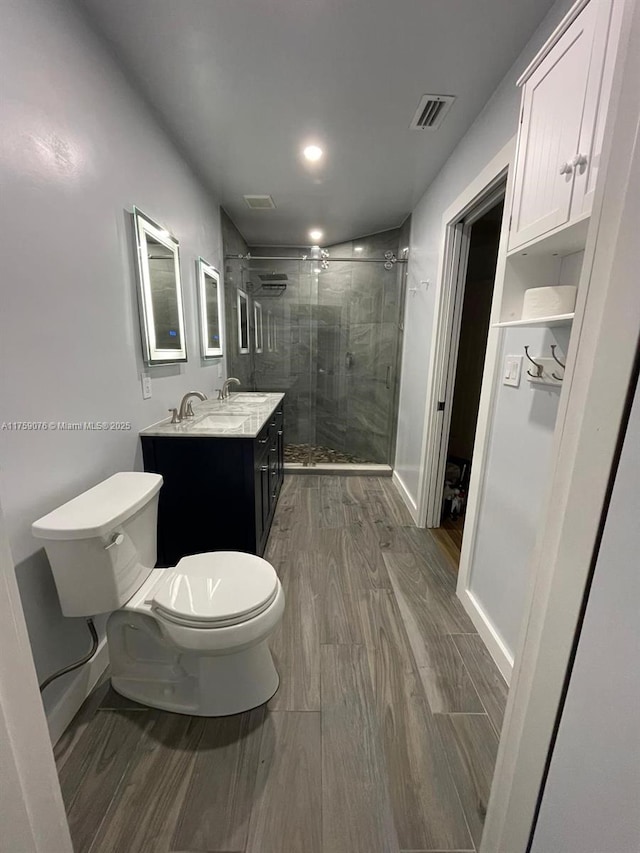 bathroom with visible vents, a shower stall, wood tiled floor, toilet, and vanity