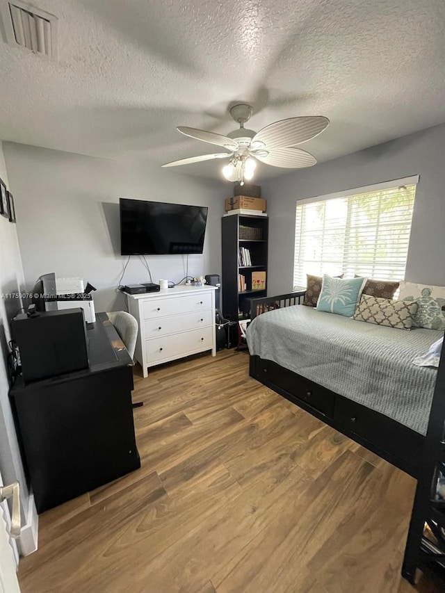 bedroom with a ceiling fan, wood finished floors, visible vents, and a textured ceiling