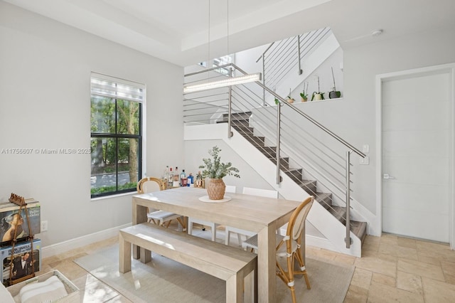 dining room with stone tile floors, stairway, a tray ceiling, and baseboards