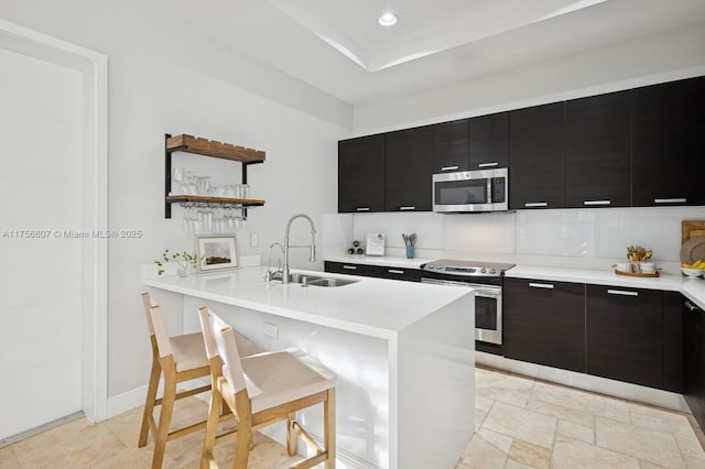 kitchen with a sink, open shelves, dark cabinetry, stainless steel appliances, and light countertops