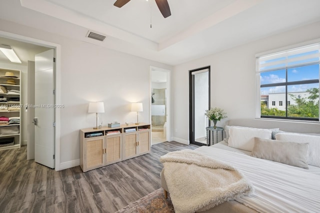 bedroom featuring a tray ceiling, wood finished floors, visible vents, and baseboards