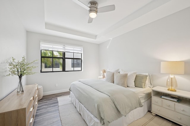 bedroom with a tray ceiling, baseboards, light wood-type flooring, and ceiling fan