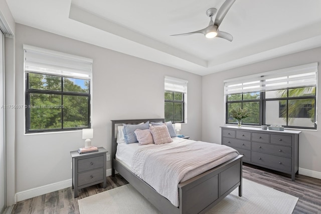 bedroom with a ceiling fan, a raised ceiling, wood finished floors, and baseboards