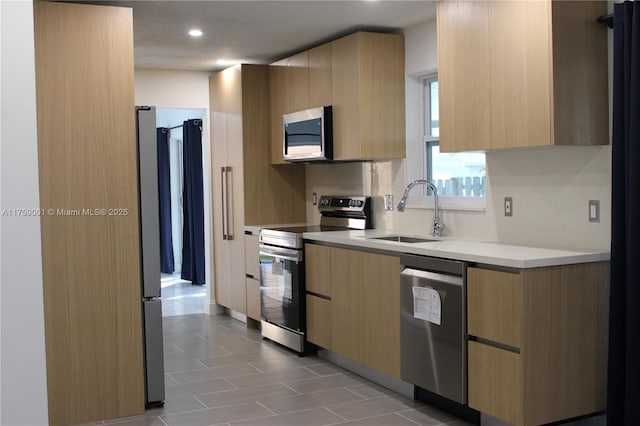 kitchen with a sink, light brown cabinetry, light countertops, stainless steel appliances, and modern cabinets