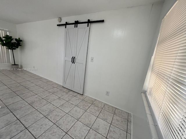 empty room with a barn door and light tile patterned floors