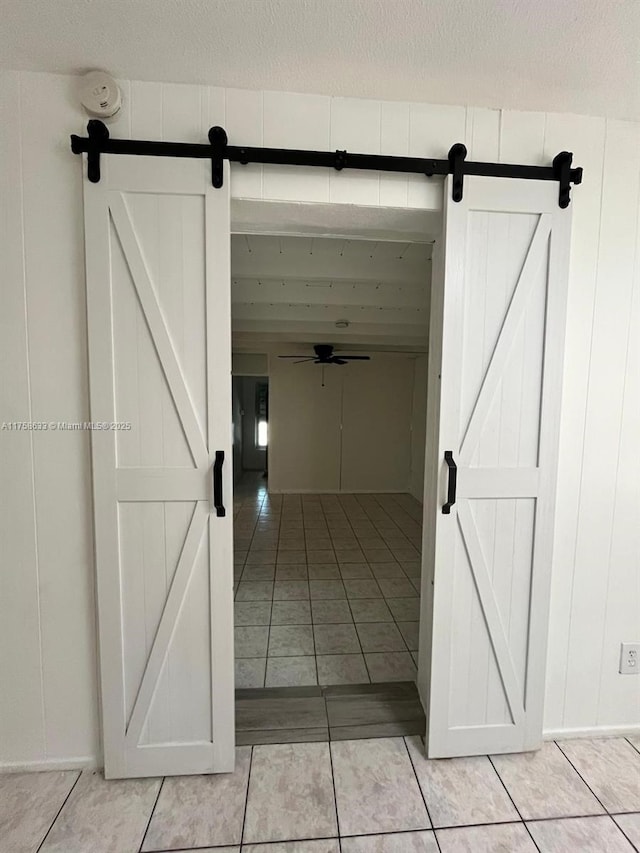 hall featuring light tile patterned floors, a textured ceiling, and a barn door