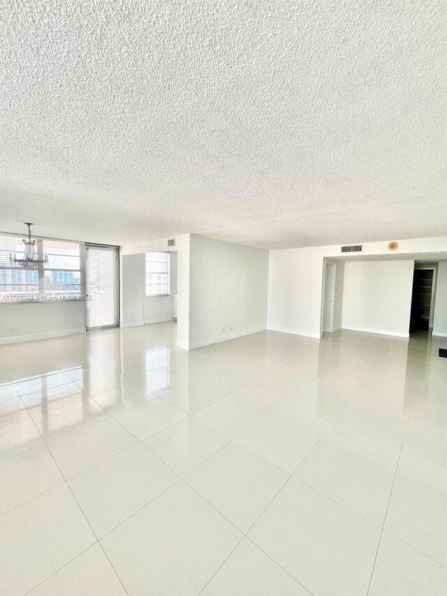 empty room with tile patterned floors, visible vents, a textured ceiling, and baseboards