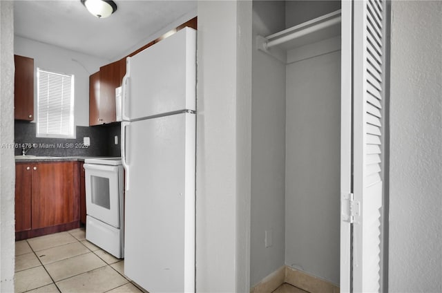 kitchen featuring white appliances, light tile patterned floors, a sink, decorative backsplash, and dark countertops