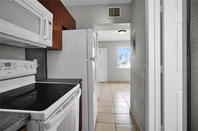 kitchen featuring visible vents, dark countertops, white appliances, light tile patterned floors, and baseboards