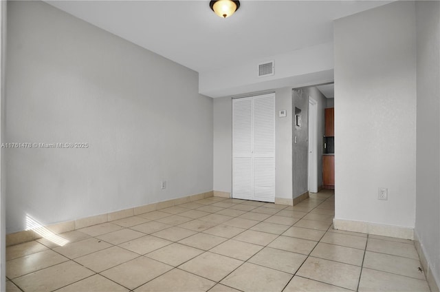 empty room with light tile patterned floors, visible vents, and baseboards