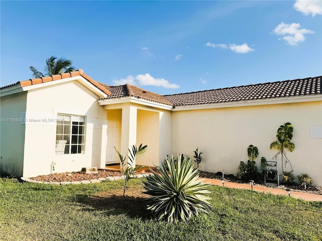 view of front of house featuring a tile roof, a front yard, and stucco siding