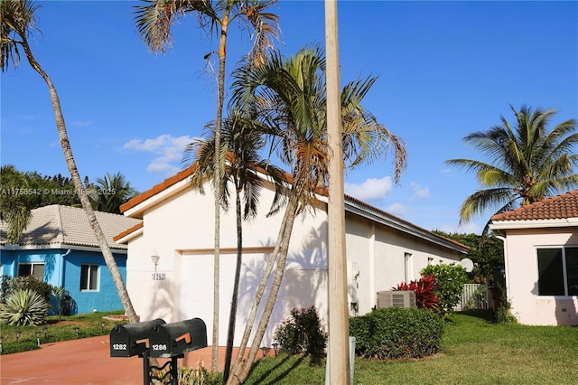 view of side of home with central air condition unit, an attached garage, a lawn, and stucco siding