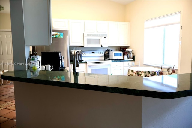 kitchen featuring tile patterned flooring, white appliances, white cabinets, and a peninsula