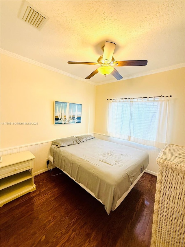 bedroom featuring wood finished floors, a wainscoted wall, visible vents, a textured ceiling, and crown molding