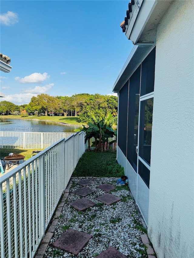 view of side of property featuring fence, a water view, a sunroom, and stucco siding