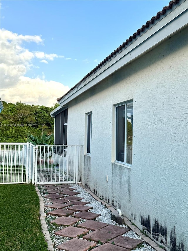 view of side of home featuring stucco siding, a tile roof, and fence