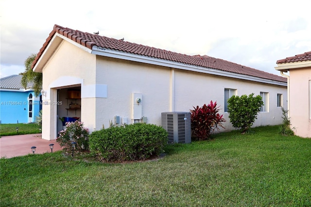 view of side of property with a tiled roof, central AC unit, a lawn, and stucco siding