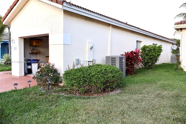 view of side of property with a tiled roof, a yard, central AC unit, and stucco siding