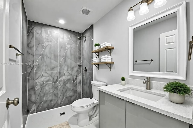 bathroom with visible vents, toilet, vanity, and a tile shower