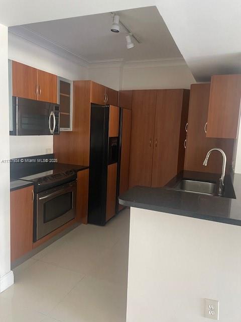 kitchen featuring a sink, dark countertops, stainless steel appliances, brown cabinetry, and glass insert cabinets