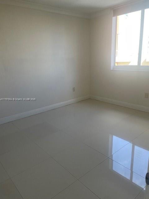 spare room featuring tile patterned flooring, baseboards, and ornamental molding