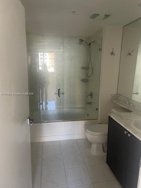 bathroom with tile patterned floors, toilet, vanity, and shower / bath combination with glass door