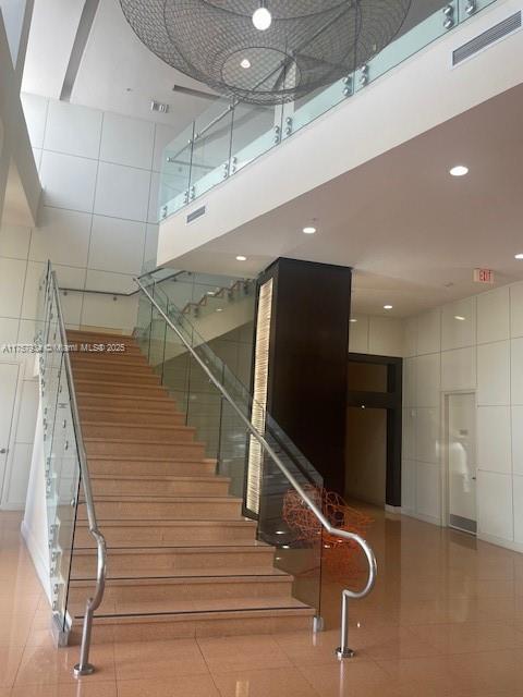 stairway with tile patterned floors, visible vents, recessed lighting, a high ceiling, and tile walls