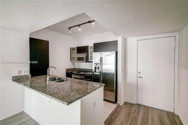 kitchen with dark stone countertops, a peninsula, a sink, stainless steel appliances, and light wood-type flooring