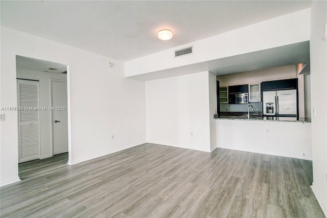 unfurnished living room featuring a sink, visible vents, baseboards, and wood finished floors