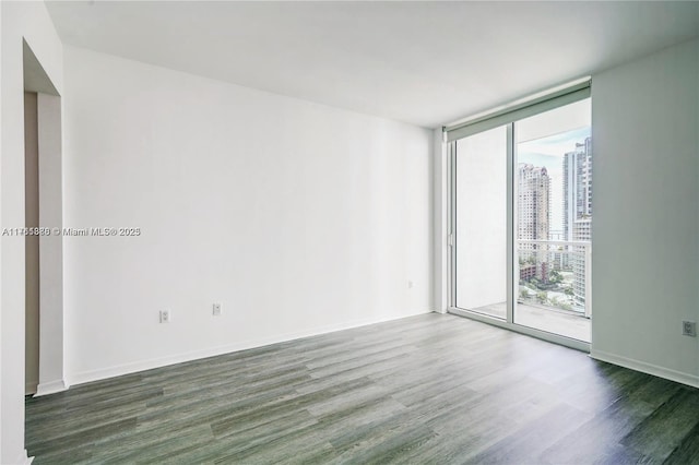 empty room with a city view, a wall of windows, wood finished floors, and baseboards